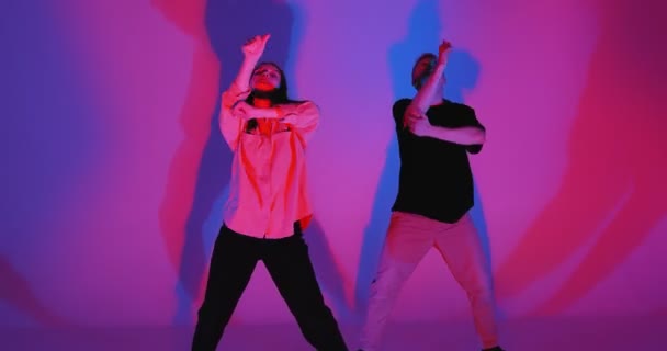 Dançando jovem casal legal se movendo na luz do estúdio de néon colorido. Dança contemporânea, performance de dançarinos de hip hop — Vídeo de Stock