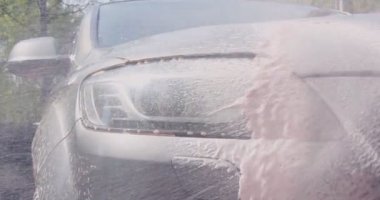 Yüksek basınçlı çamaşır makinesiyle araba temizleme. Araba kaputuna ve farına köpük püskürten bir işçi. Videoyu kapat