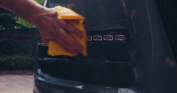 Αρσενικό χέρι χρησιμοποιώντας υγρό πανί σκουπίστε τη σκόνη από το μέρος του αυτοκινήτου. Οπίσθιο φως αυτοκινήτου καθαρισμού μολυσμένη επιφάνεια, γυαλιστικό αυτοκινήτου — Αρχείο Βίντεο