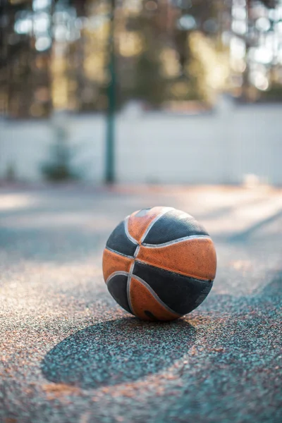 Bola de basquete deitada na superfície da quadra ao ar livre sob a luz solar. Foto publicitária para loja de equipamentos esportivos — Fotografia de Stock