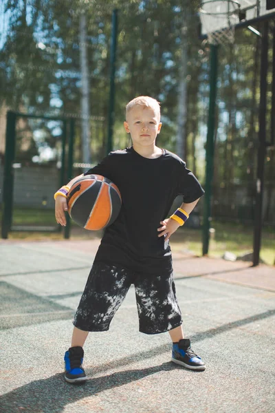 Elegante desportivo confiante menino com bola de basquete na quadra à luz do sol. Estilo de vida ativo de crianças saudáveis — Fotografia de Stock