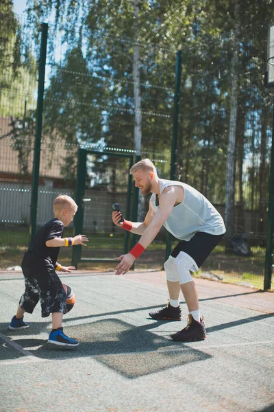 Profissional jogador de basquete instrutor treinar menino, segurando o telefone na mão, levando vídeo para redes sociais — Fotografia de Stock