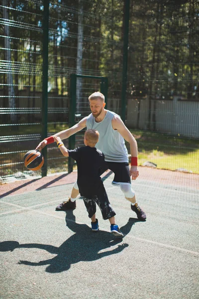 Профессиональный американский баскетболист инструктор тренирует маленького спортивного мальчика на открытом воздухе на баскетбольной площадке — стоковое фото