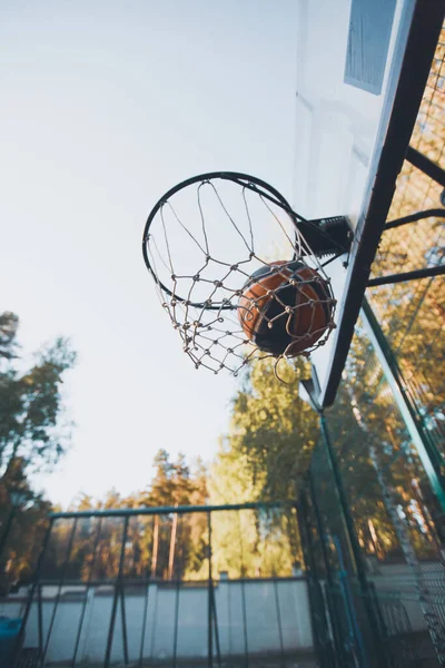 Balón de baloncesto en aro de baloncesto con red en la cancha al aire libre en verano en la naturaleza. Concepto de meta y puntería — Foto de Stock