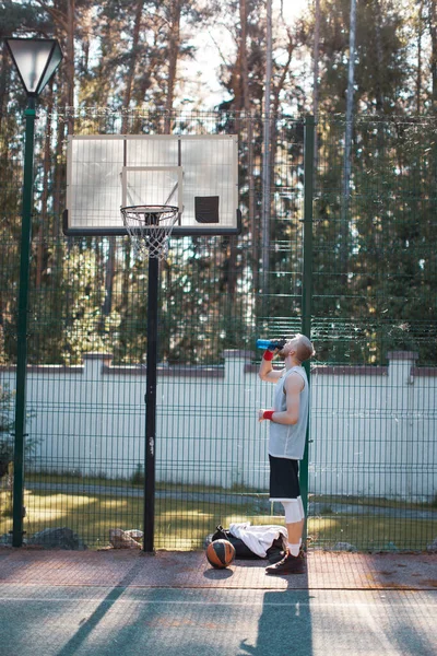 Jogador de basquete americano masculino profissional bebendo água na quadra ao ar livre no verão à luz do sol — Fotografia de Stock