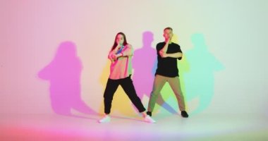 Dans eden genç çift renkli neon renkli stüdyo ışıklarıyla hareket ediyor. Dans okulu için çağdaş dans videosu