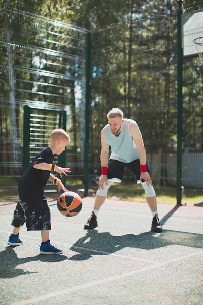 Американские баскетболисты атлетический инструктор и его ученик маленький мальчик в действии на баскетбольной площадке. Дриблинг — стоковое фото