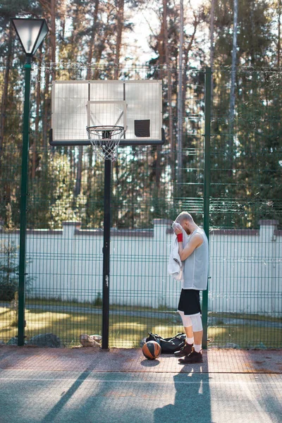 Jogador de basquete americano masculino profissional limpe seu rosto com uma toalha após o treinamento na quadra ao ar livre no verão — Fotografia de Stock