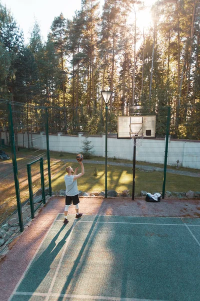 Basketball player training on court outdoors in summer on nature. Cool guy with ball exercising — Foto de Stock