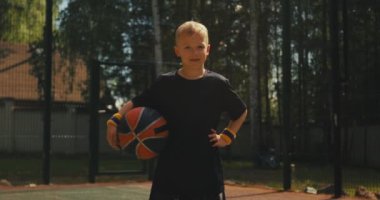 Basketbol topu taşıyan sporcu çocuk dışarıda basketbol sahasında gülümsüyor. Aktif sağlıklı çocuk yaşam tarzı