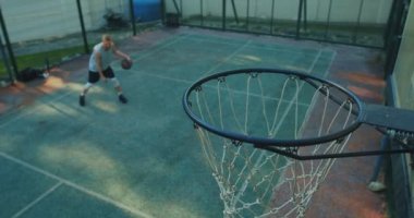 Basketbolcu, sahada antrenman yapan genç adam dışarıda basketbol potasına top atmayı hedefliyor.