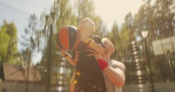 Jugadores de baloncesto deporte feliz familia padre e hijo de entrenamiento con pelota en la cancha de baloncesto. Papá ayudar a niño anotando aro — Vídeos de Stock