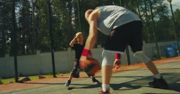 Профессиональный американский баскетболист инструктор тренирует маленького спортивного мальчика дриблинг к воротам на открытом воздухе на баскетбольной площадке — стоковое видео