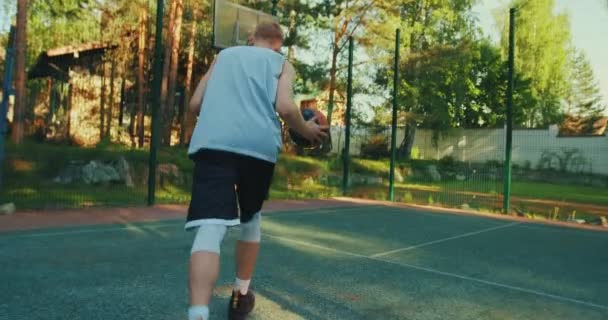 Masculino americano basquete jogador formação no tribunal jogando bola no basquete aro ao ar livre, visão traseira — Vídeo de Stock