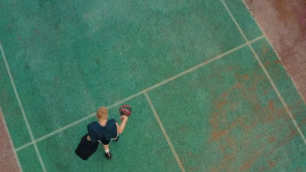 Vista aérea del jugador de baloncesto que comienza el entrenamiento, anotando aro en la cancha de baloncesto al aire libre — Vídeos de Stock