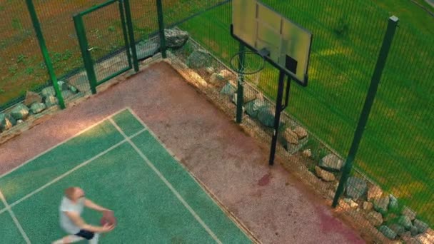 Lanzamiento aéreo de cancha de baloncesto. Vista aérea del jugador de baloncesto acercándose, anotando aro durante el entrenamiento al aire libre — Vídeos de Stock