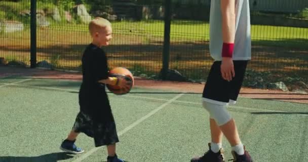 Basketbalspeler sport mannelijke instructeur opleiding kind jongen te dribbelen op basketbal veld buiten in de zomer. — Stockvideo