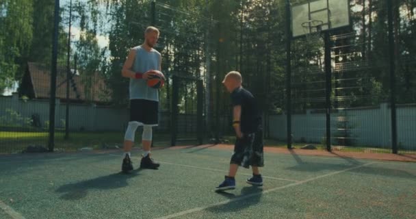 Jugadores de baloncesto. Familia deportiva. Niño niño espectáculo handstand ejercicio con padre en baloncesto cancha en sol — Vídeos de Stock