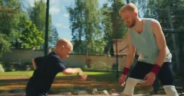 Basketballer sportlicher Typ trainiert Jungen im Sommer zum Dribbeln auf dem Basketballplatz — Stockvideo