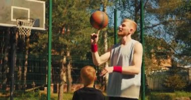 Erkek basketbol oyuncusu sportif eğitmen, çocuk çocuğa dışarıda antrenman yaparken sahada top çevirmeyi öğretiyor.