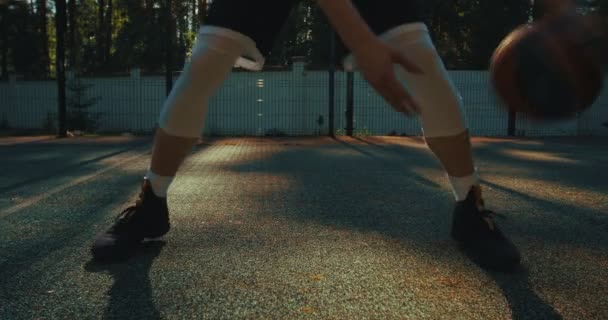 Мужчина-баскетболист, практикующий навыки обращения с мячом, дриблинг мяч между ног на площадке во время тренировки летом — стоковое видео