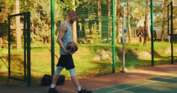 Крутой молодой парень спортсмен баскетболист пойти на корт и забить мяч в обруч на открытом воздухе летом — стоковое видео