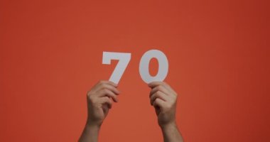 Yetmiş numara ellerinde. Oy vermek ya da matematik öğrenmek için oylanmış kağıttan 70 haneli rakamlar gösteren bir adam.