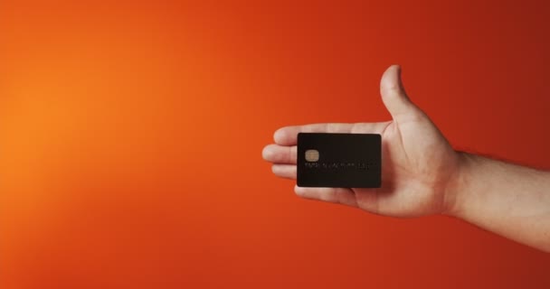 Close up male hand showing levitating template mockup Bank credit card with online service isolated on orange background — Stock Video