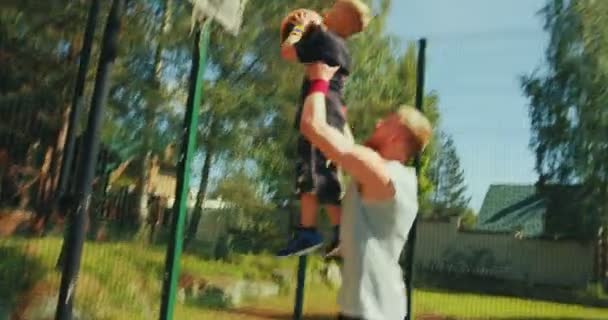 Jovem pai esportivo com filho em mãos jogando basquete. Kid boy jogando bola no basquete aro ao ar livre — Vídeo de Stock