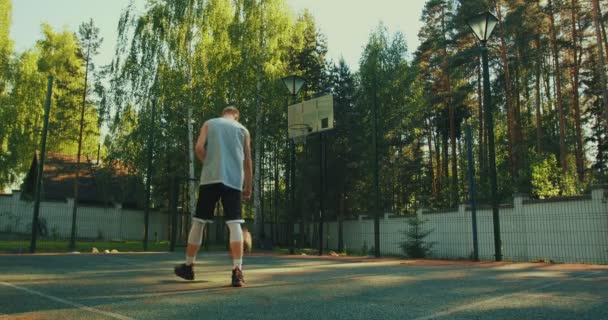 उन्हाळ्यात कोर्टाच्या मैदानी हॉपमध्ये थंड तरुण पुरुष बास्केटबॉल खेळाडू चेंडू स्कोअर करीत आहे — स्टॉक व्हिडिओ