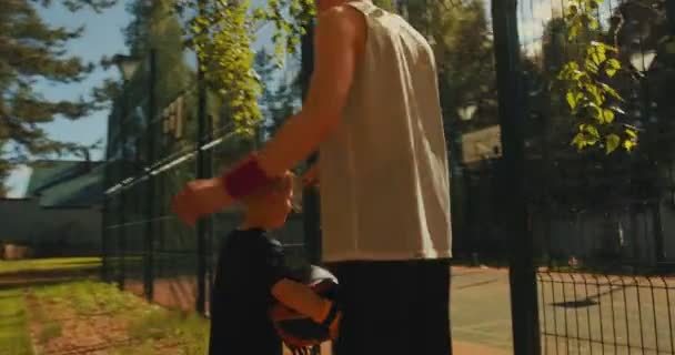 Basketballer männlich sportlich Kerl und Kind Junge gehen gemeinsam zum Training auf Basketballplatz im Freien bei Sonnenschein — Stockvideo