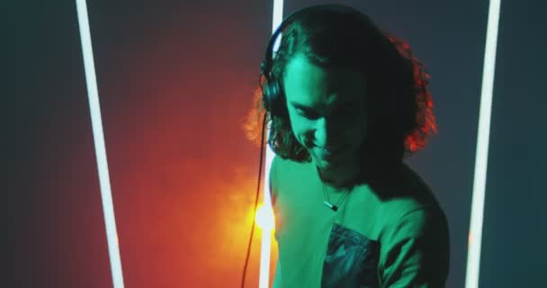 Cool młody facet DJ w słuchawki słuchać dj pop muzyka taniec w kolorowe światło studio podczas rave — Wideo stockowe