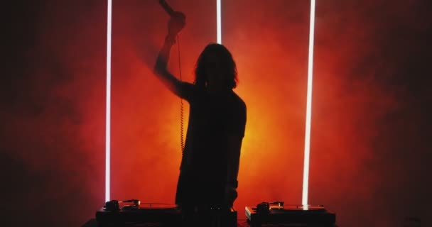 Silhouette of male dj playing music at nightclub, raising up hand with headphones in sunset orange light. Nightlife — Stock Video