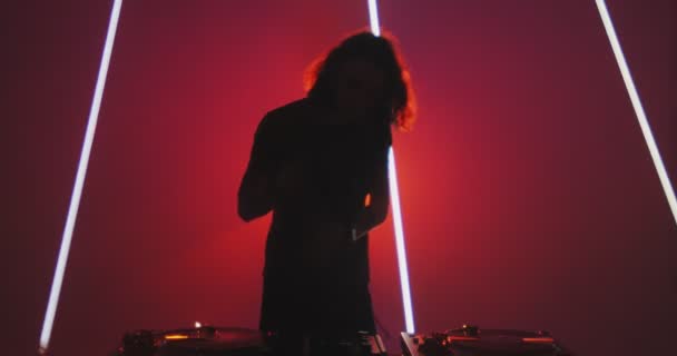 DJ cool τύπος που παίζει μουσική που δείχνει φώτα κατά τη διάρκεια της παράστασης κοντά στην κονσόλα DJ στο νυχτερινό κέντρο διασκέδασης. Σύγχρονη μουσική rave — Αρχείο Βίντεο
