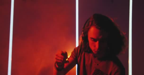 Bailando DJ chico guay con auriculares se enciende en la discoteca durante la actuación en el club nocturno. Moderna rave — Vídeos de Stock