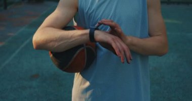 Close-up male basketball player with ball looking at smart watch with app for online workout on basketball court