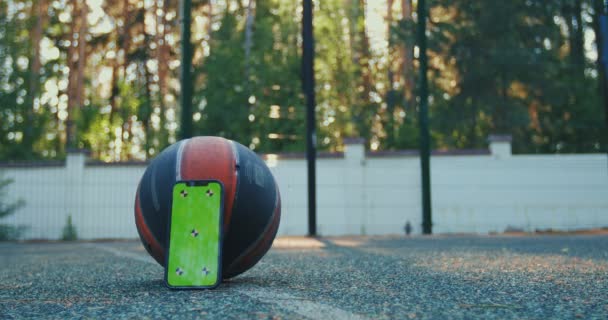Макет телефона с зеленым экраном с отслеживающими маркерами, баскетбольным мячом и спортивной обувью на корте. Ключевой смартфон Chroma — стоковое видео
