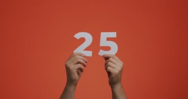 25 numara ellerinde. Rakamları gösteren bir adam, oylama ya da matematik öğrenmek için oyulmuş kağıttan yapılmış 25 kişi.