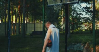 Sporcu erkek basketbolcu antreman sırasında telefonla konuşuyor. Basketbol sahasında güneş ışığında yürüyor.