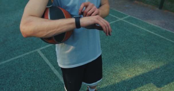 Detailní mužský basketbalista při pohledu na chytré hodinky s aplikací pro online cvičení na basketbalovém hřišti — Stock video