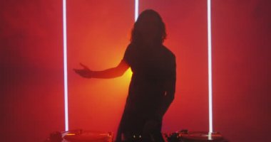 Dans eden DJ 'in silueti gece kulübünde kırmızı ışıkta sallanan genç adam. Gece hayatı konsepti