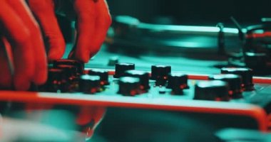 DJ, gece kulübü partisinde mikser masasında elektronik müzik çalıyor. DJ elleri kaydıraklara dokunuyor. Yakın plan.