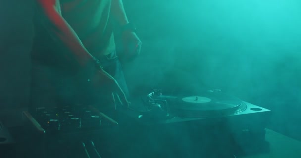 Deejay haciendo girar discos en el tocadiscos bailando en el humo en el club nocturno. Dj actuando en fiesta, música electrónica moderna rave — Vídeo de stock