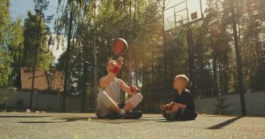 Spor mutlu bir aile. Erkek basketbolcu baba, dışarıda basketbol sahasında topu parmaklarıyla döndürmeyi öğreniyor.