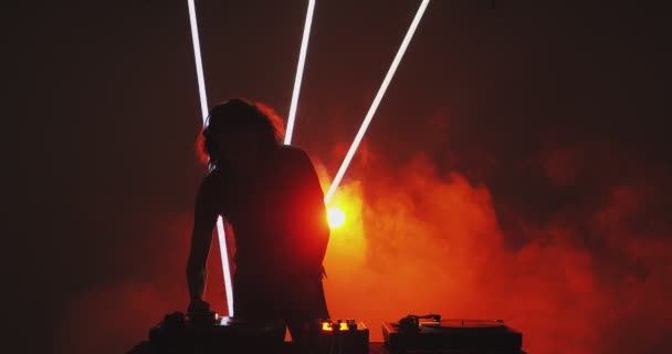 Uma rave de DJ quente. Silhueta de DJ legal jovem tocando música na plataforma giratória em luz vermelha em fumaça na boate — Vídeo de Stock