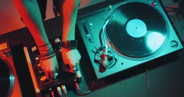 Deejay curseurs touchants jouant de la musique électronique sur la plaque tournante dans la soirée de boîte de nuit dans la lumière colorée. Vue du dessus — Video