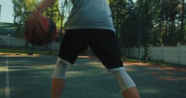 Erkek basketbolcu sahada bacaklarının arasına top sürüyor basketbol sahasında basketbol antrenmanı sırasında basket atıyor.