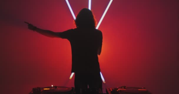 Deejay cooler Kerl während eines Auftritts in der Nähe einer DJ-Konsole in einem Nachtclub mit Neonlampen. Musikalisch modernes Rave-Konzept — Stockvideo