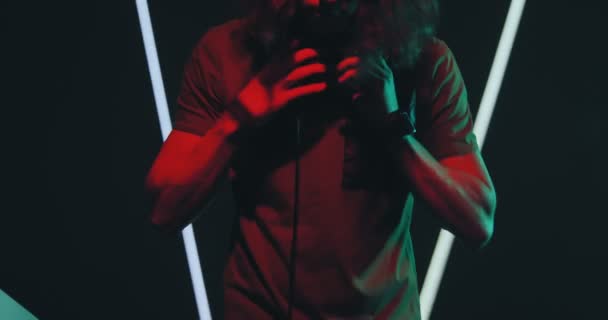 Cool deejay het dragen van een koptelefoon het afspelen van elektronische muziek in nachtclub op feest in kleurrijk licht. Nachtleven — Stockvideo