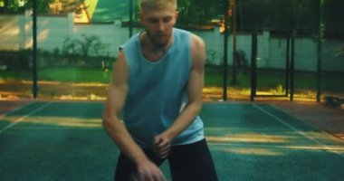 Havalı genç basketbolcu top sürüyor ve dışarıda basketbol sahasında kameraya atıyor.